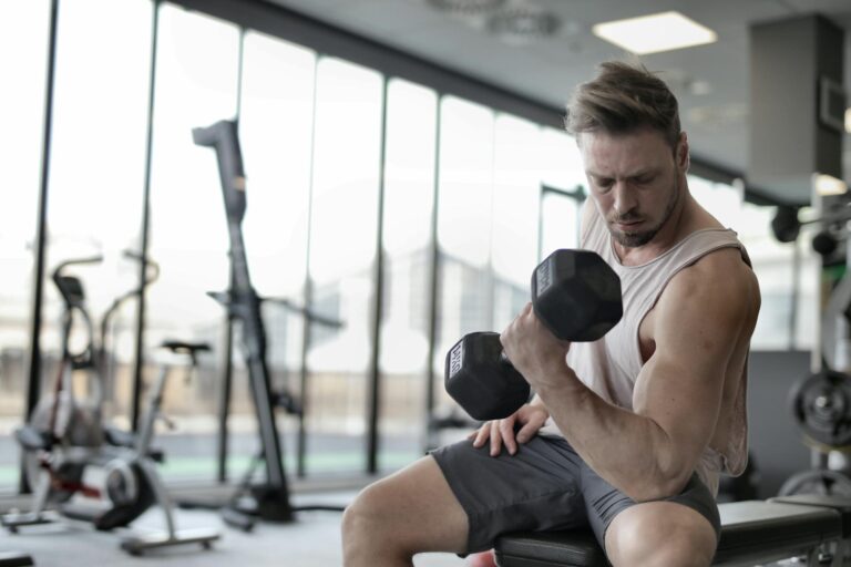 man in white tank top and grey shorts lifting dumbbell