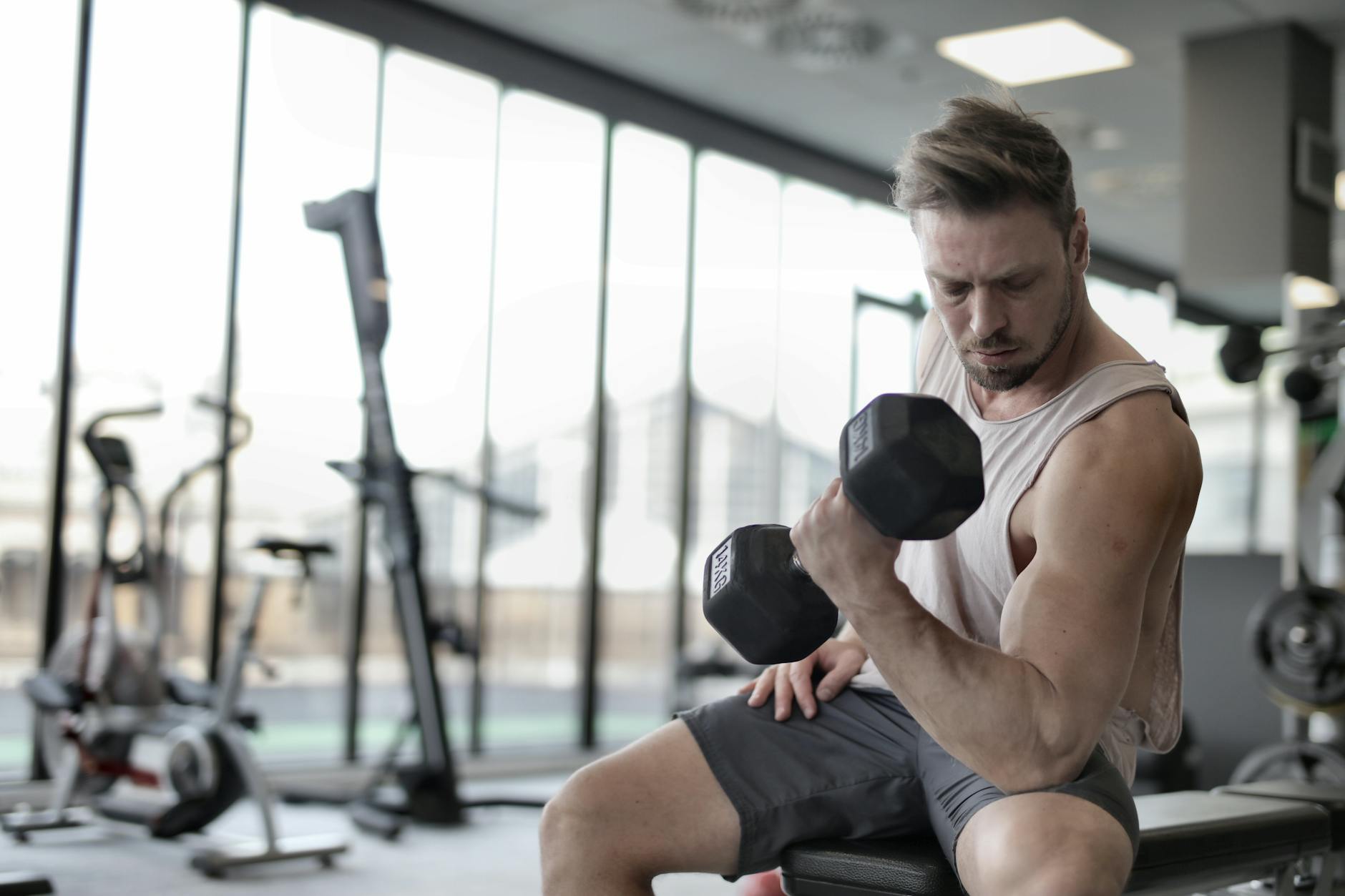 man in white tank top and grey shorts lifting dumbbell