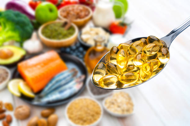 Close up view of a metal spoon filled with Omega-3 capsules shot against defocused food rich in Omega-3 acid like salmon, sardines, avocado, and nuts. , gut health